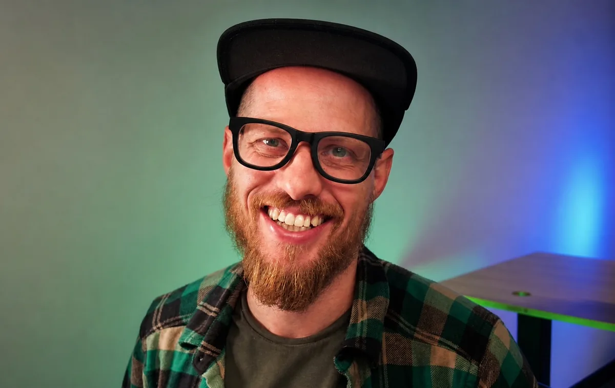 Kevin Kirchner smiling, in black glasses, a black cap and a green plaid shirt