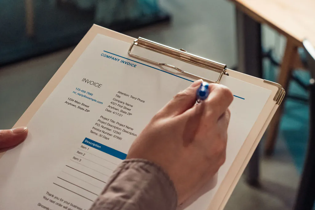 A hand fills in a blank invoice on a clipboard, the bill that still has to go out after the job