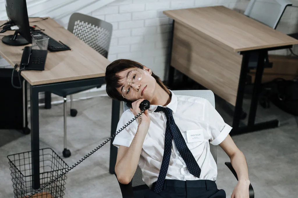 A worn-out office worker slumped in a desk chair with the desk phone at their ear, another status call in a long day
